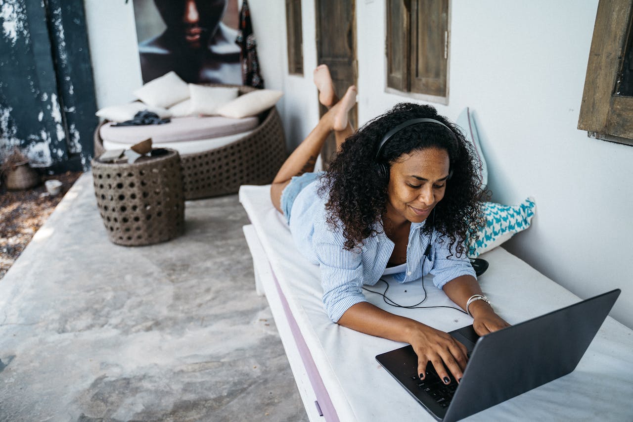 Woman enjoying remote work outdoors on a laptop in a relaxed setting with headset.